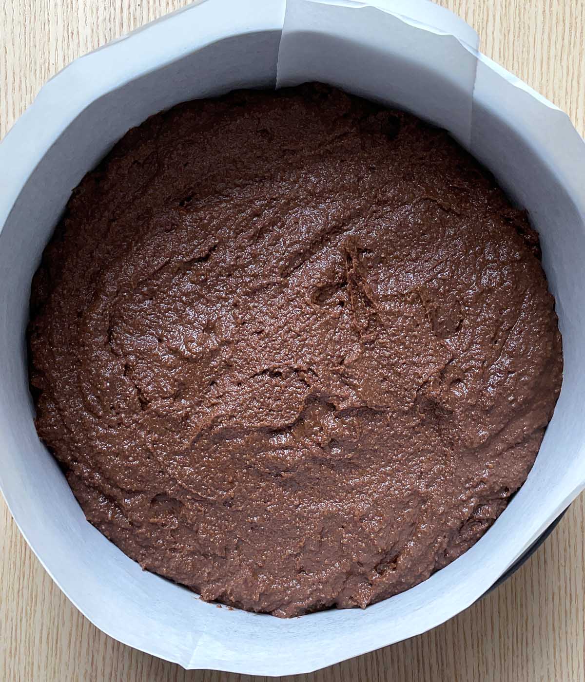 Brown cake batter in a round pan lined with white paper.