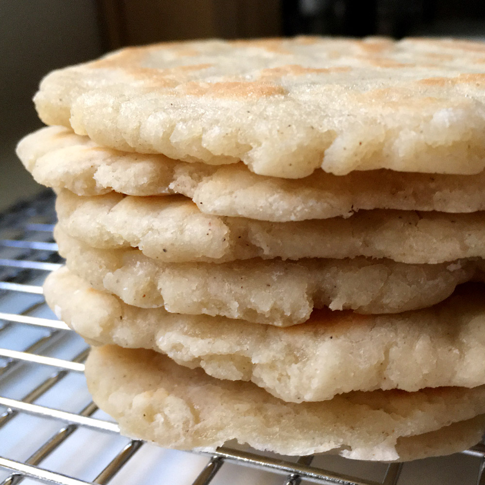 A stack of 6 light brown flatbreads on a metal rack