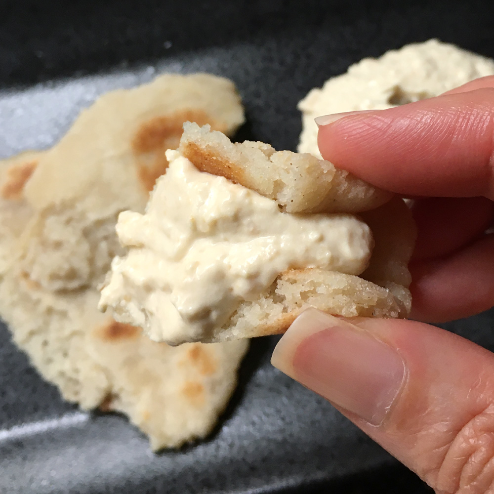 Close-up of a hand holding a piece of flatbread with light colored hummus dip