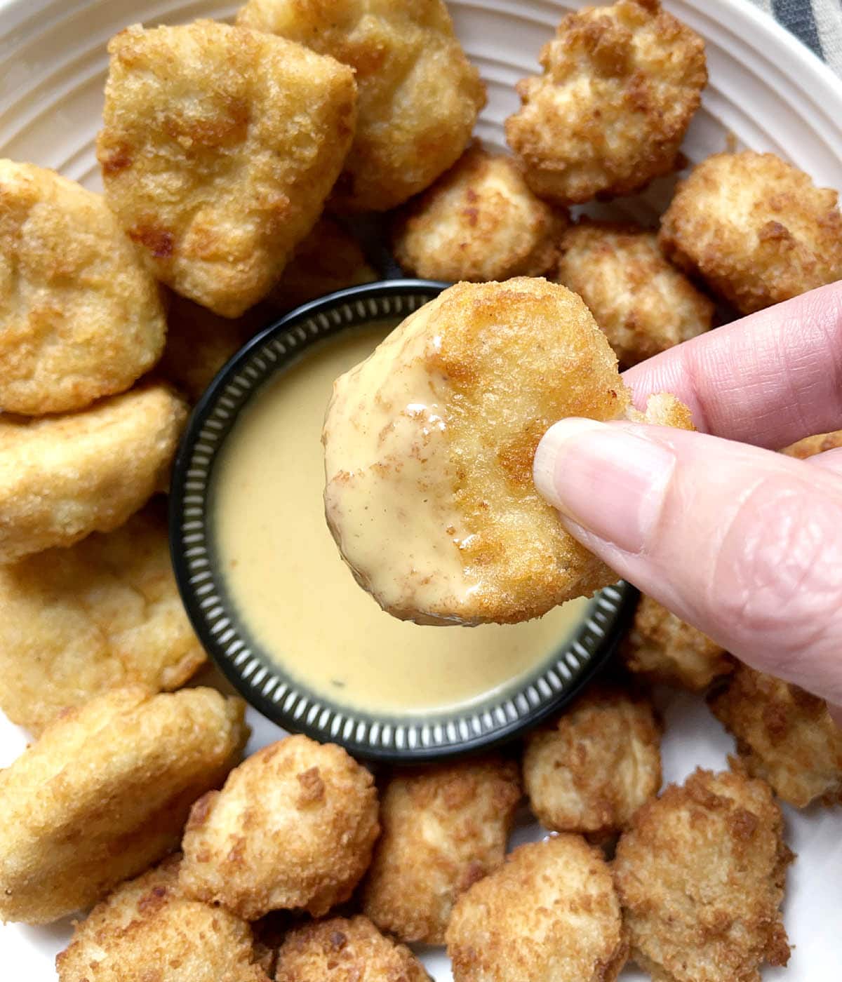 Close-up of a hand holding a breaded chicken nugget with yellow honey mustard dressing.