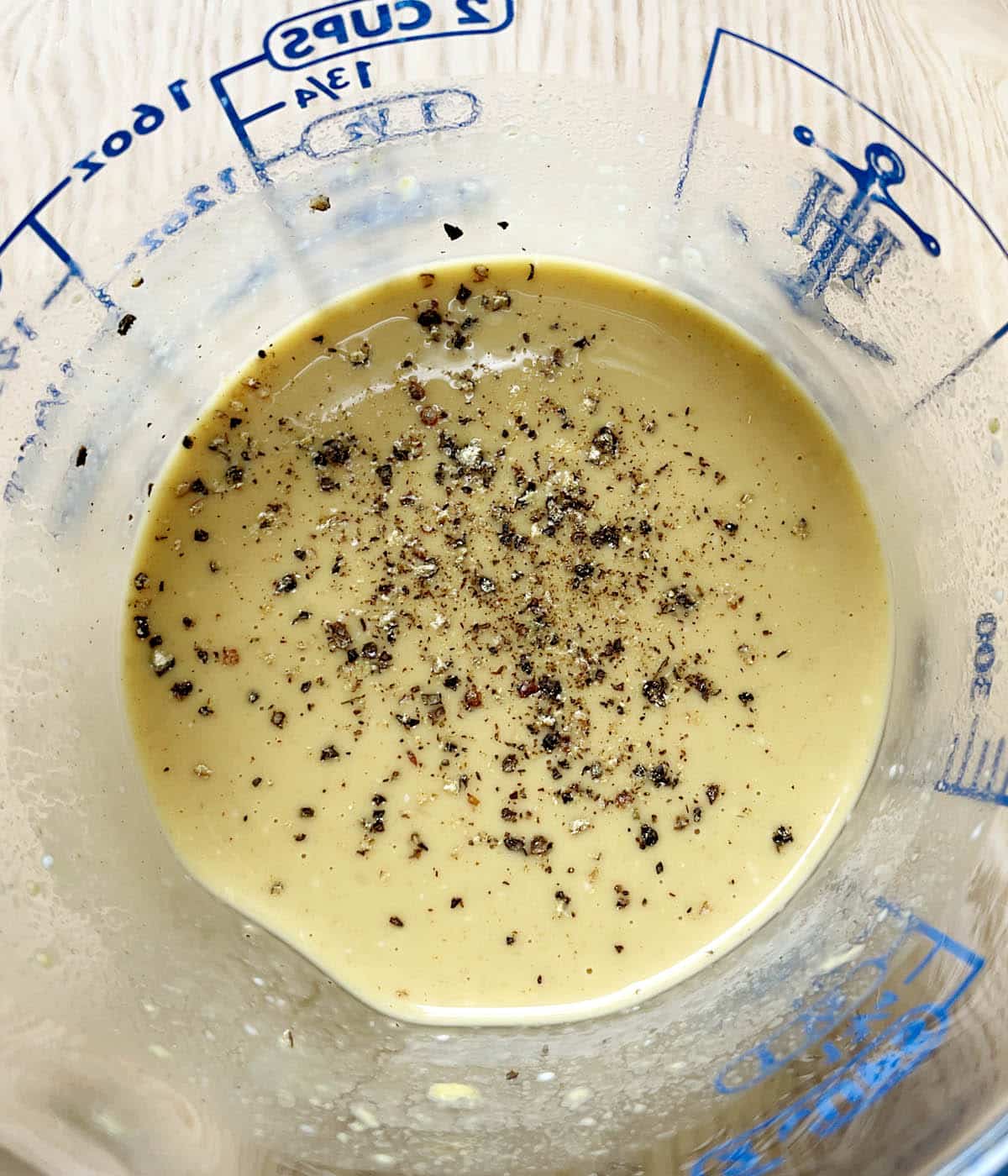 A glass measuring cup containing honey mustard dressing and black pepper.