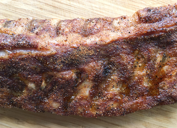 A rack of cooked ribs on a wooden cutting board