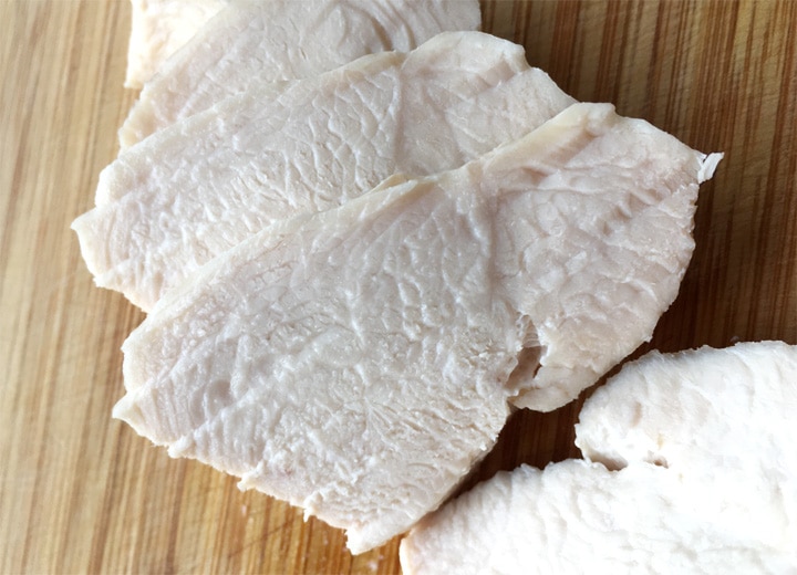 Slices of white chicken meat on a wooden cutting board