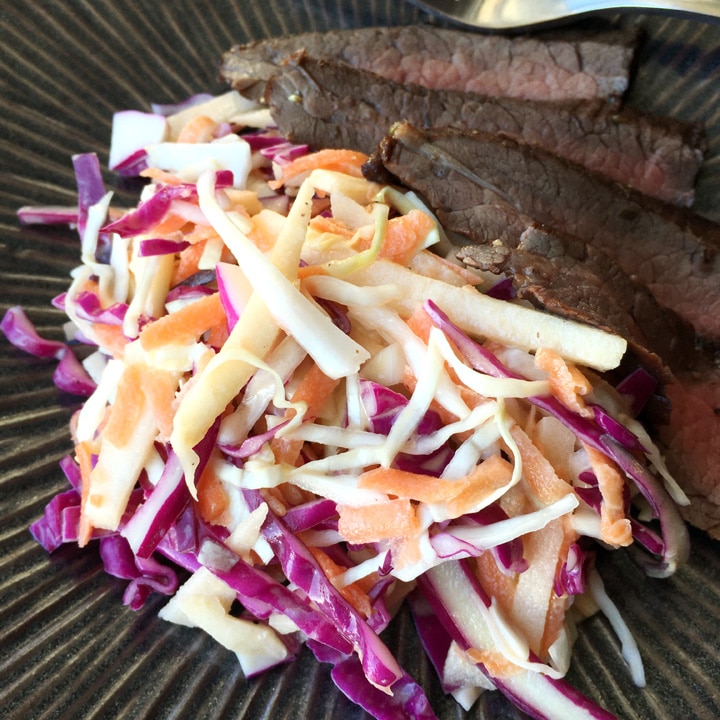 Slices of brown steak next to a mound of coleslaw on a dark plate