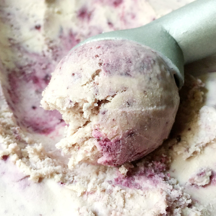 Close-up of an ice cream scoop scooping a ball of white and purple ice cream from a container