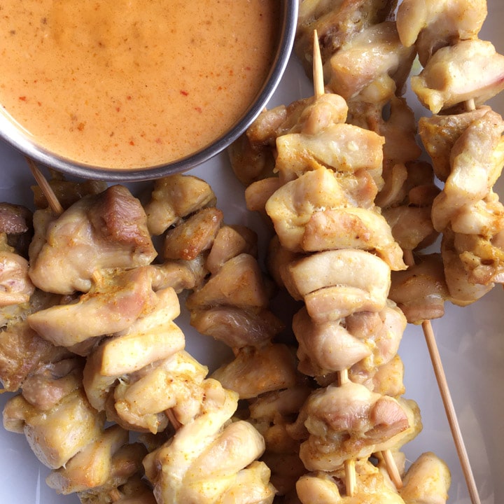 Chicken chunks on wooden skewers, next to a round bowl of orange sauce