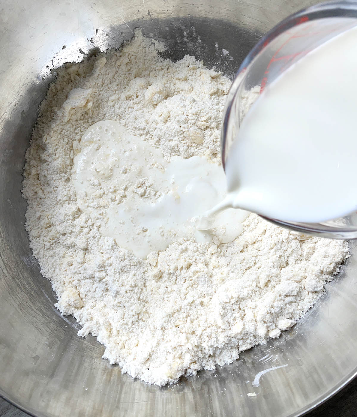 White milk being poured into a metal bowl containing white flours.