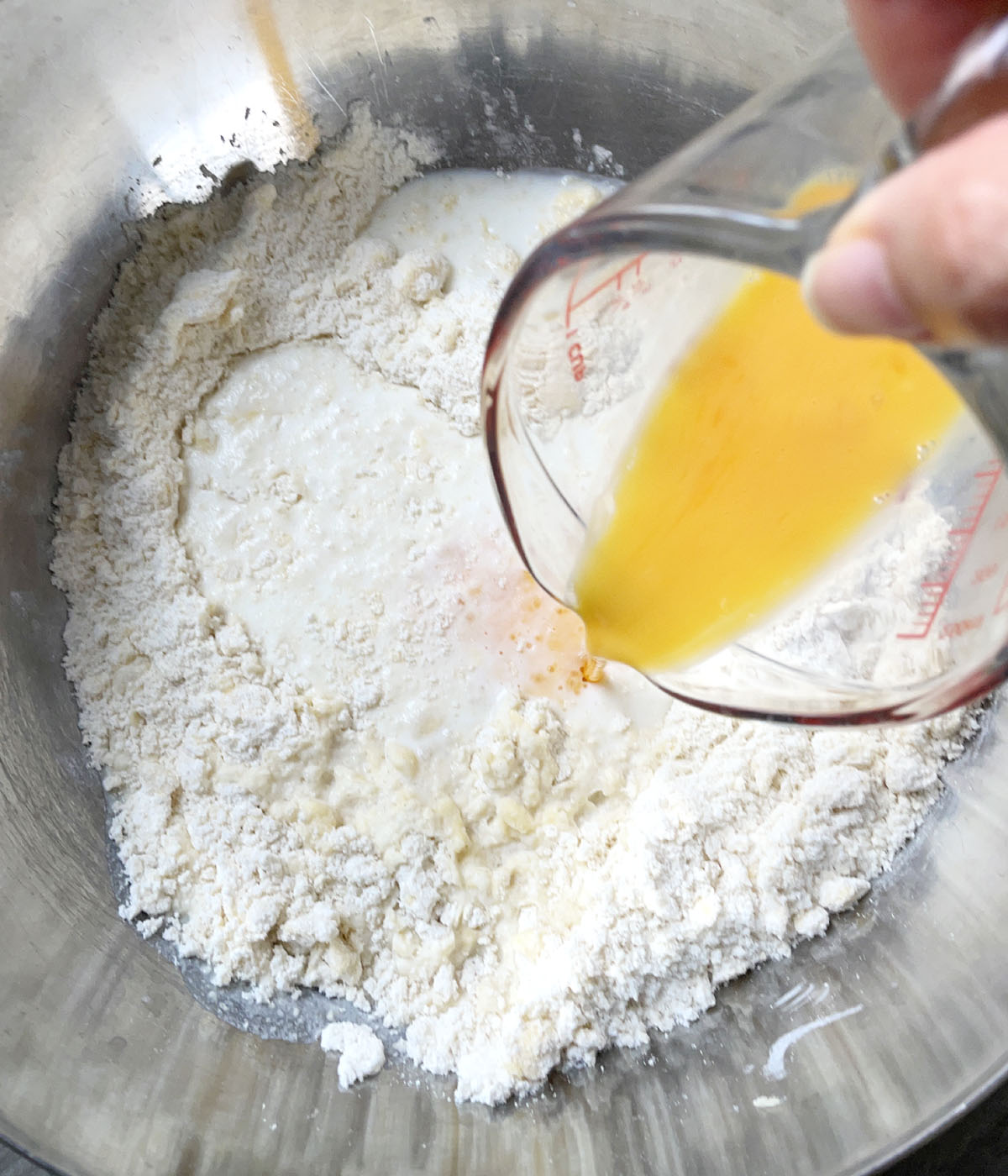 A yellow beaten egg being poured into a metal bowl containing flours and milk.