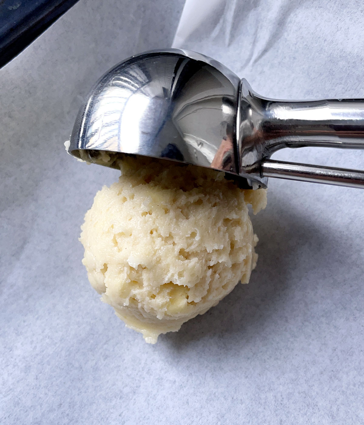 A metal scoop lifting off a scoop of scone dough on parchment paper.