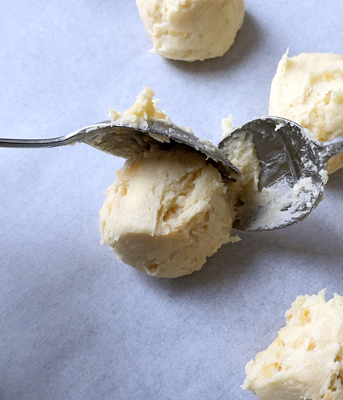Two spoons place a ball of scone dough on white parchment paper.