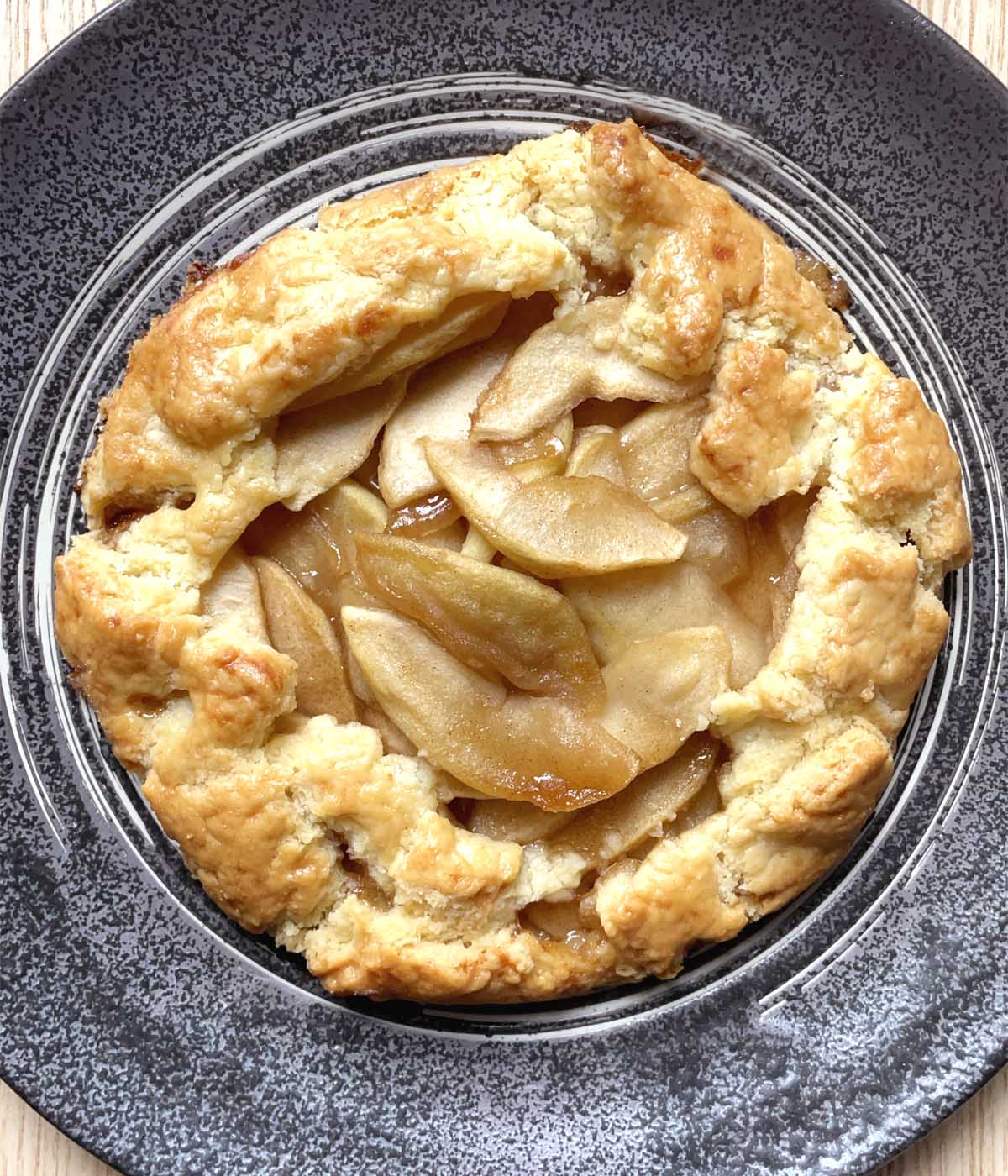 A baked apple galette with golden crust on a dark round plate.