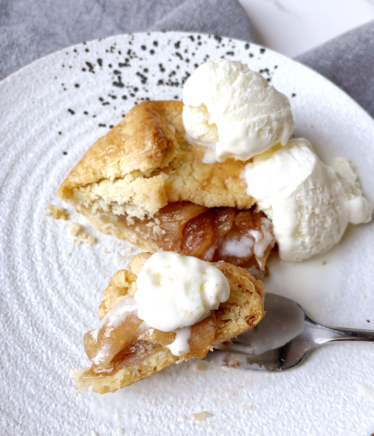 Close-up of a piece of apple galette and vanilla ice cream on a fork on a white plate.