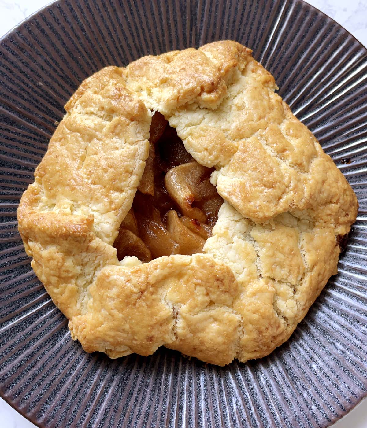 A baked apple galette on a dark brown plate.