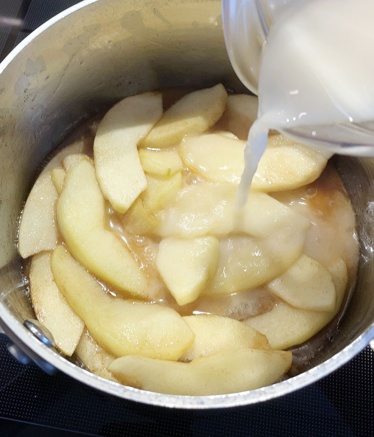 A white liquid being poured into a metal pot containing apple slices.