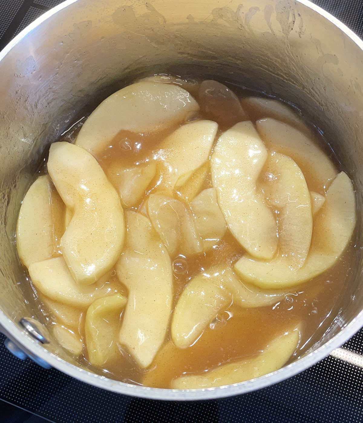 Apple slices in a brown sauce in a metal pot.