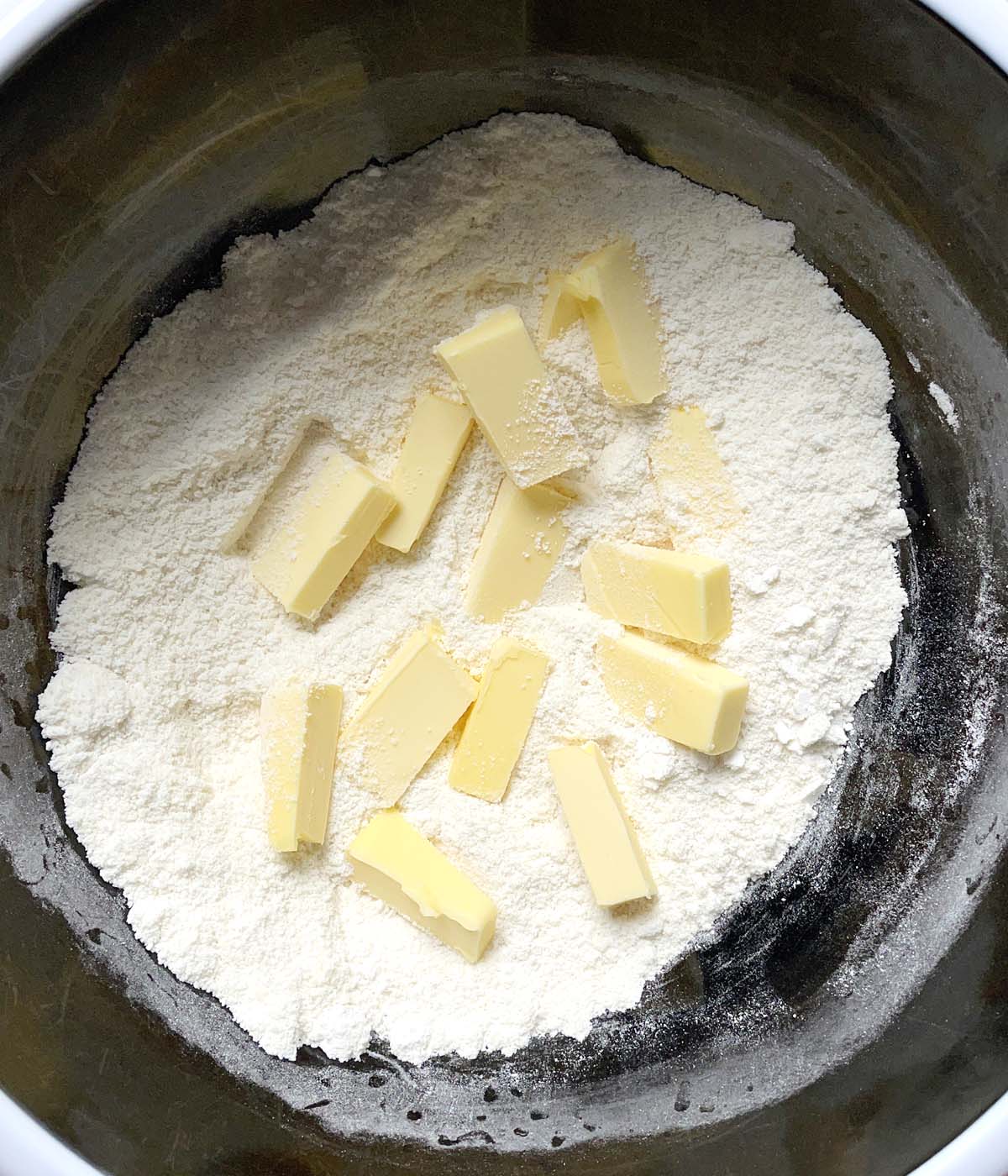 A round black bowl containing white flours and yellow butter chunks.