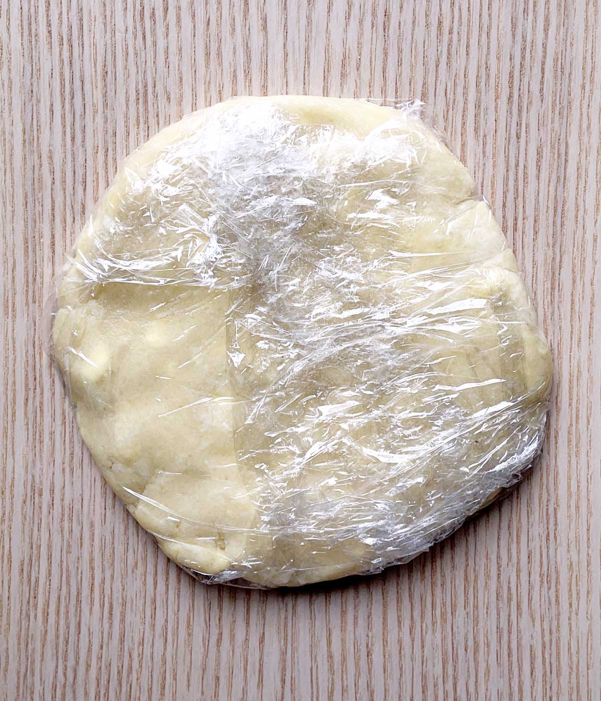 A round disc of dough wrapped in clear plastic wrap.