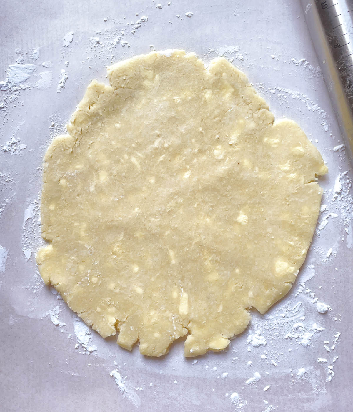 Rolled out light yellow pie crust rolled out on a flour dusted white paper.