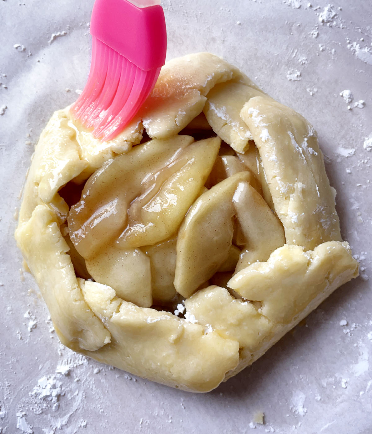 A pink brush spreading egg wash over the crust of an apple pie.