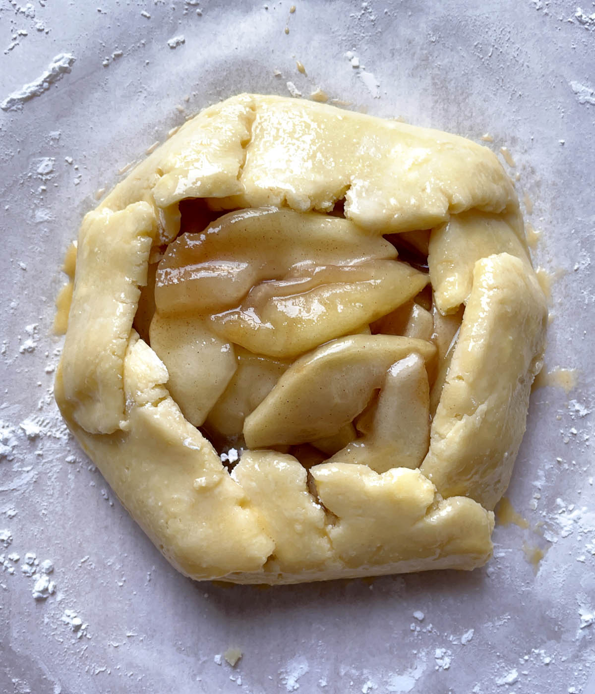 An uncooked roughly rounded apple galette with apples in the middle.