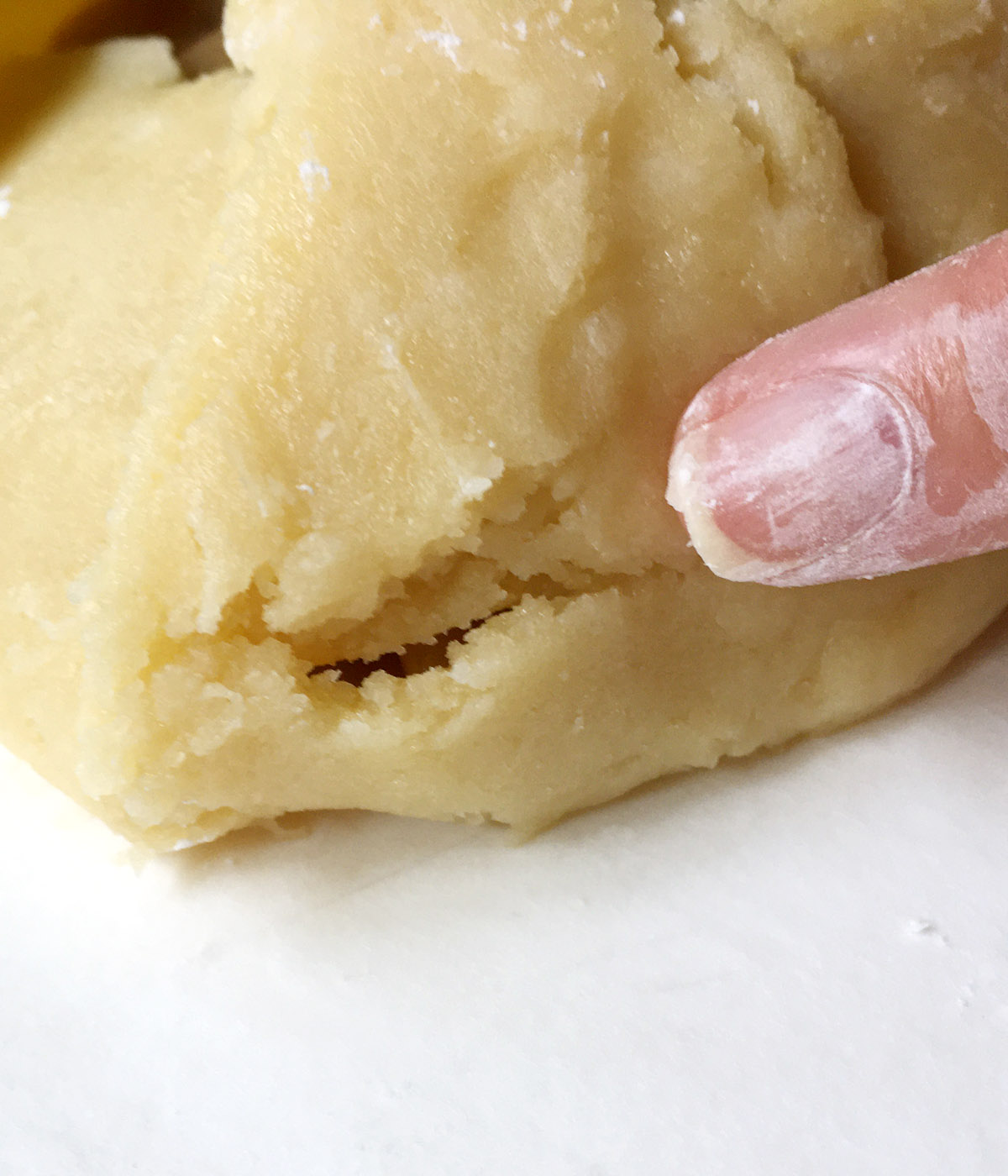 Close-up of a finger pointing to a crack in pie crust dough.