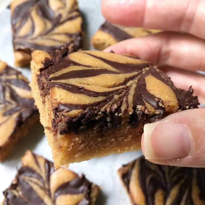 A hand holding a brown baked square with chocolate swirls