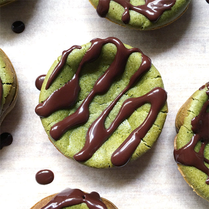 Round green cakes, drizzled with brown chocolate, on a white surface