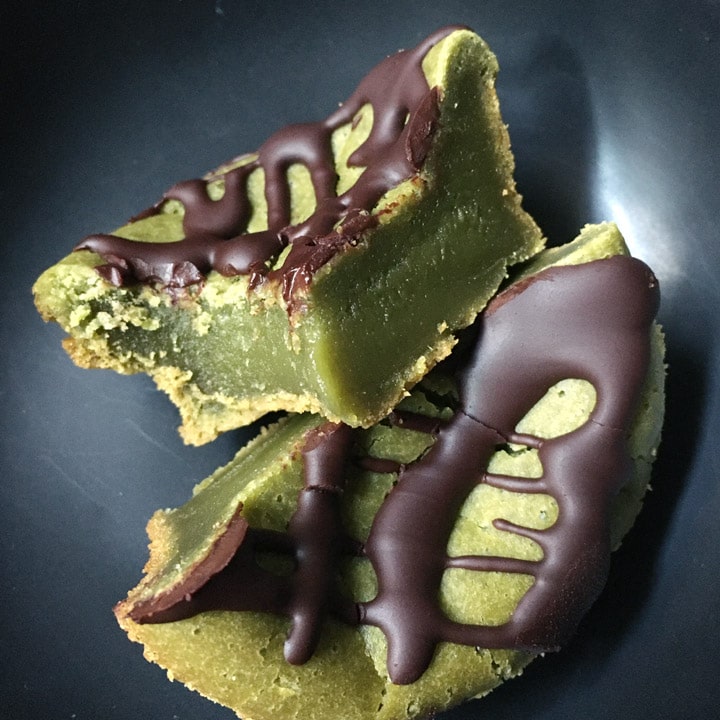 A round green cake with chocolate topping, cut in half, on a dark dish