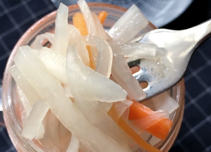 Close-up of a fork pulling white radish and orange carrot strips from a jar