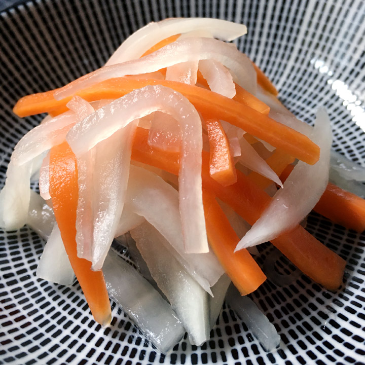 A dark blue and white round bowl containing a heap of pickled white daikon and orange carrots