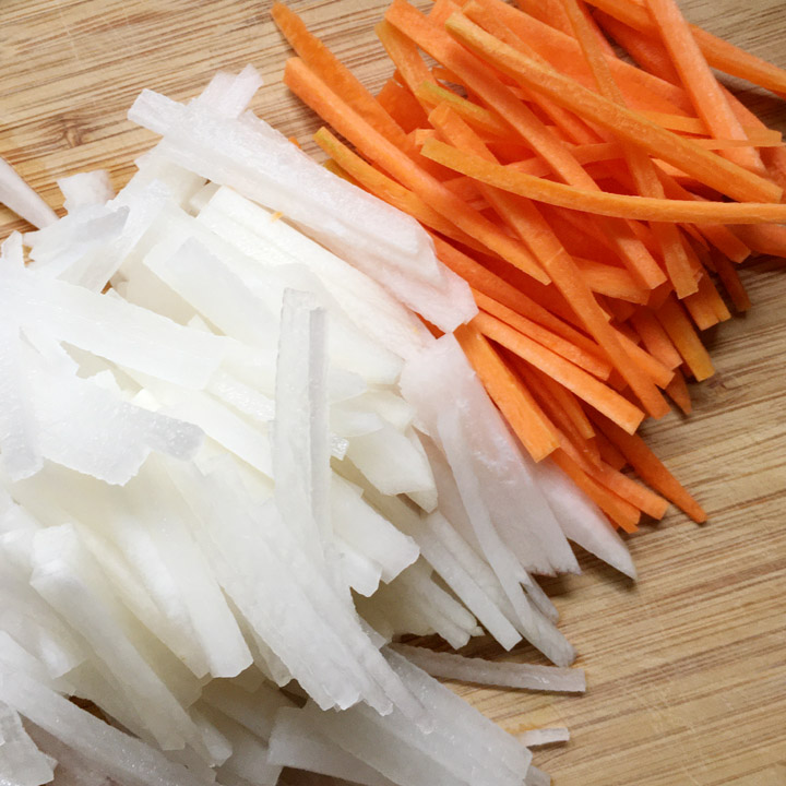 White radish and orange carrot, cut into matchsticks on a wooden cutting board