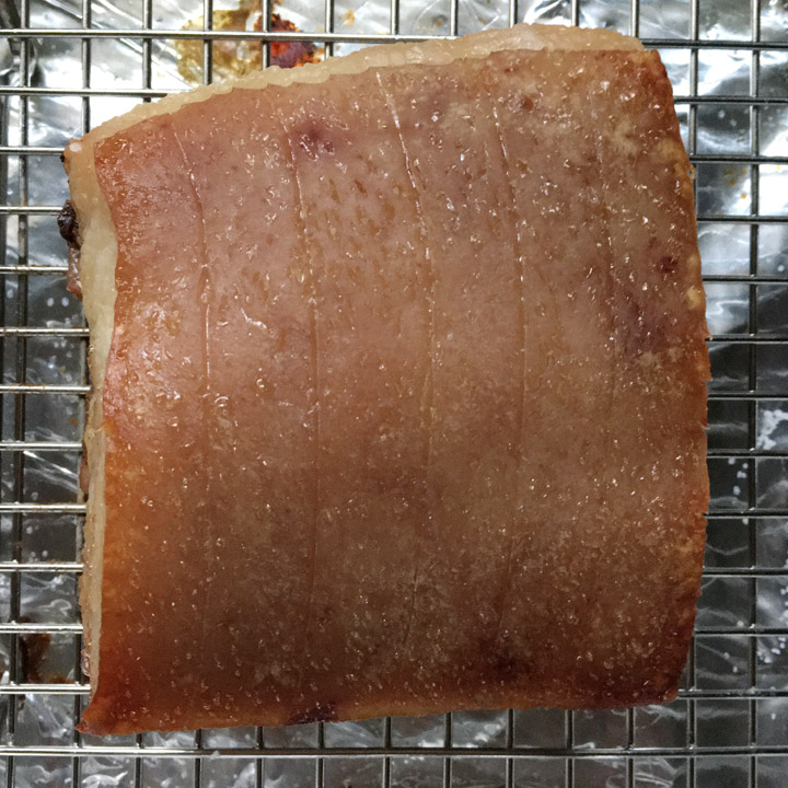 A squarish shaped piece of meat with lines scored into the skin, on a rack on a pan