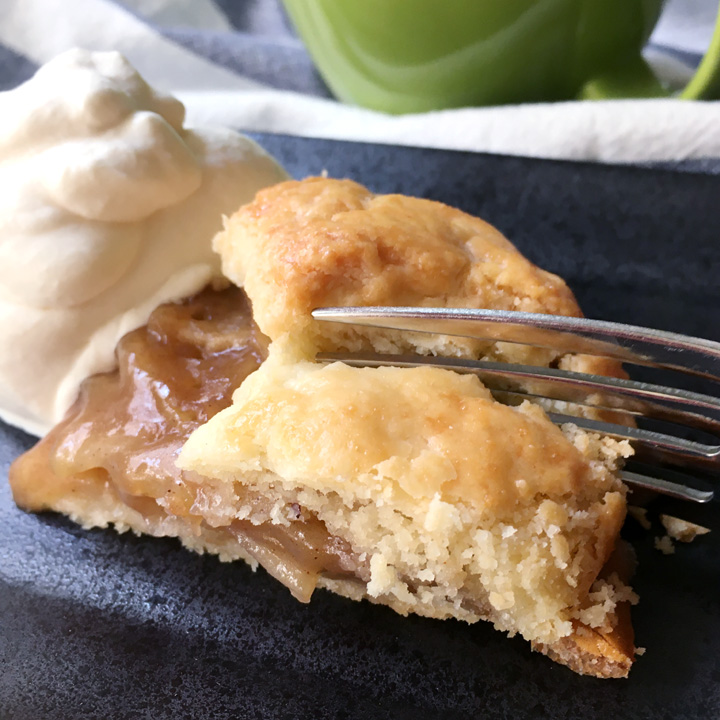 A fork cutting into a wedge shaped piece of apple galette, next to a mound of white whipped cream