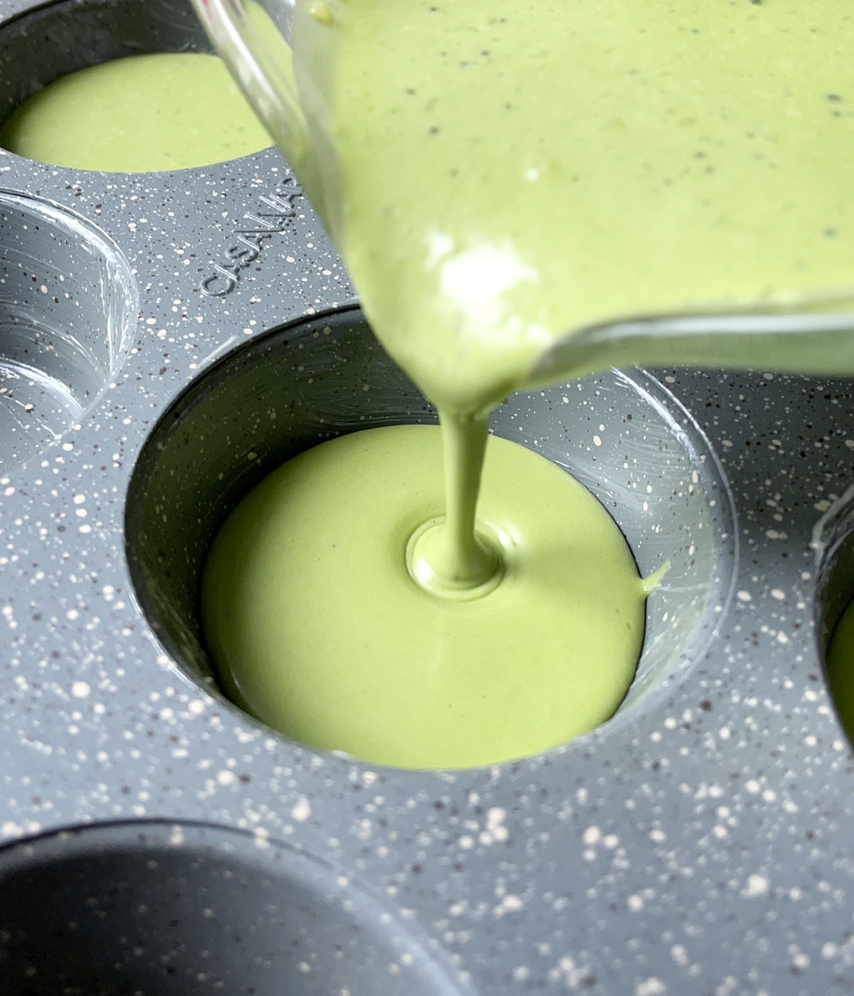 A green liquid being poured into a gray speckled muffin tin.