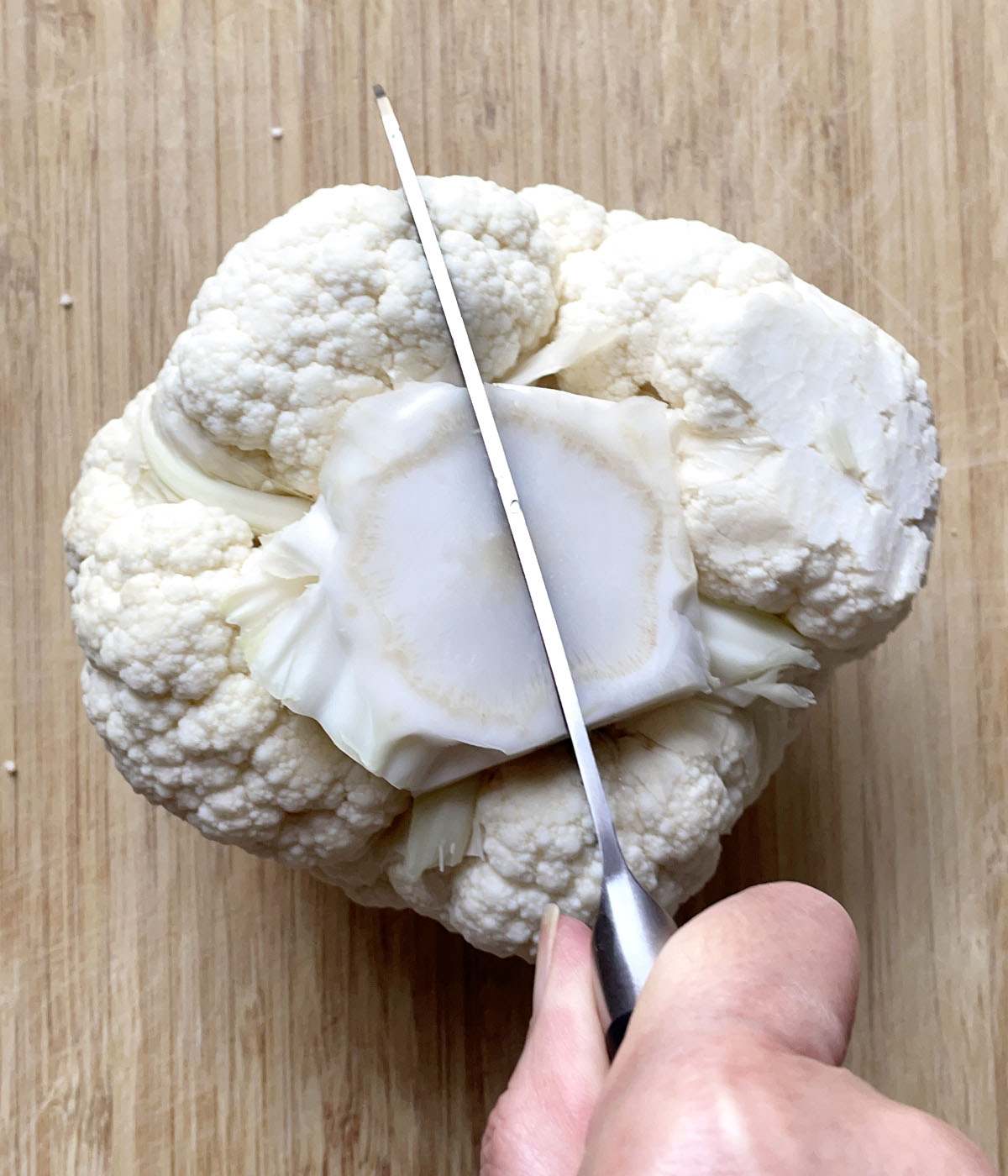 A knife cutting a head of cauliflower in half through the core.
