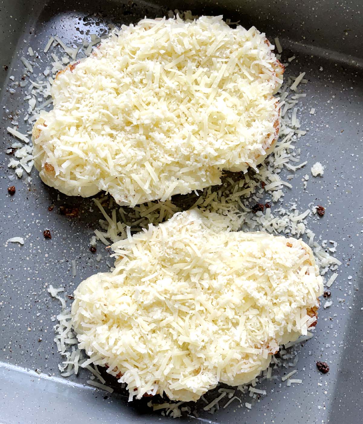 Two cauliflower steaks topped with grated parmesan cheese in a grey baking pan.