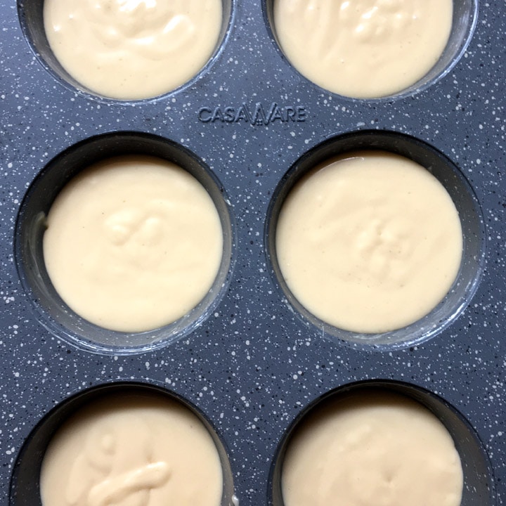 A grey muffin tin with 6 cups filled with light brown batter.