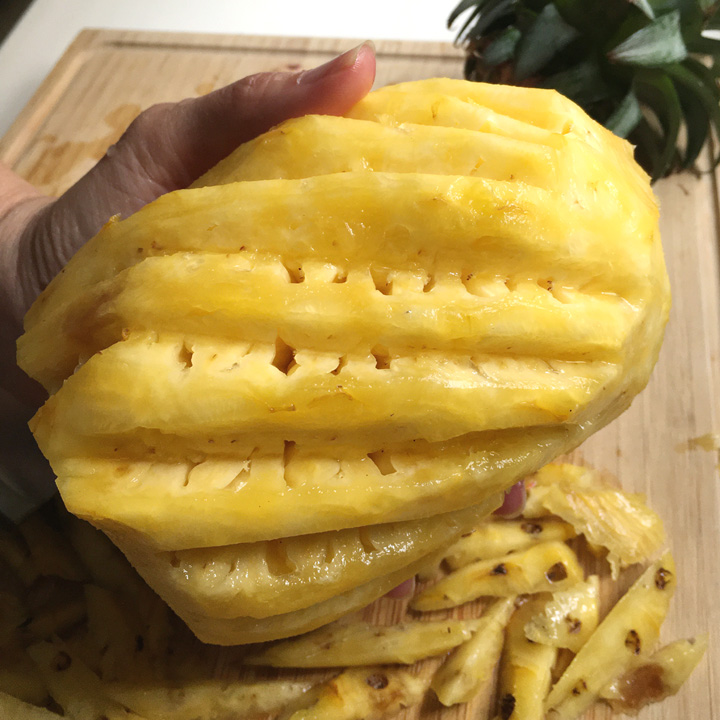A hand holding a peeled yellow pineapple