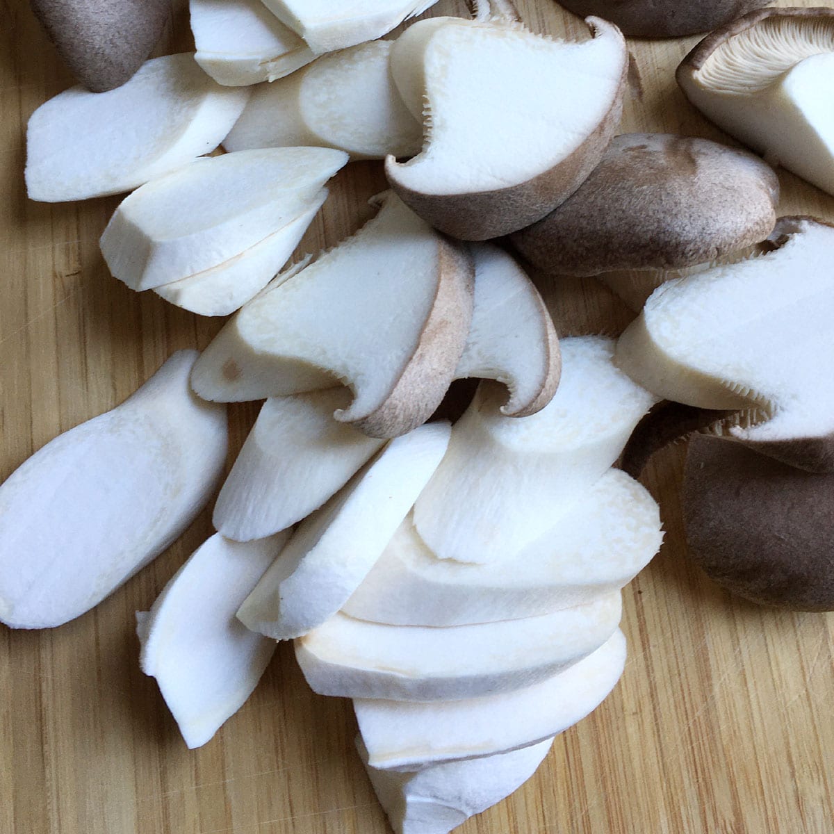 Thick slices of white and brown mushrooms on a wooden cutting board.