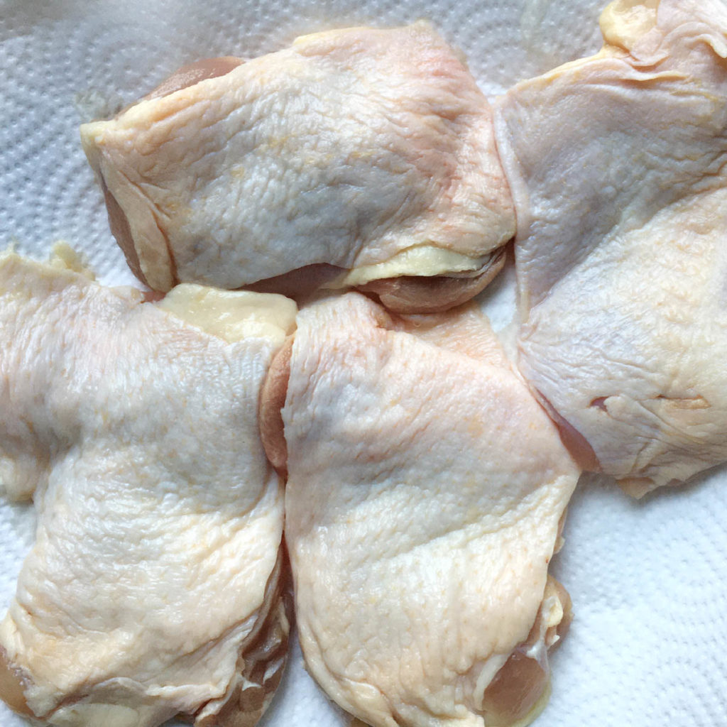 Four raw chicken pieces on a white paper towel.