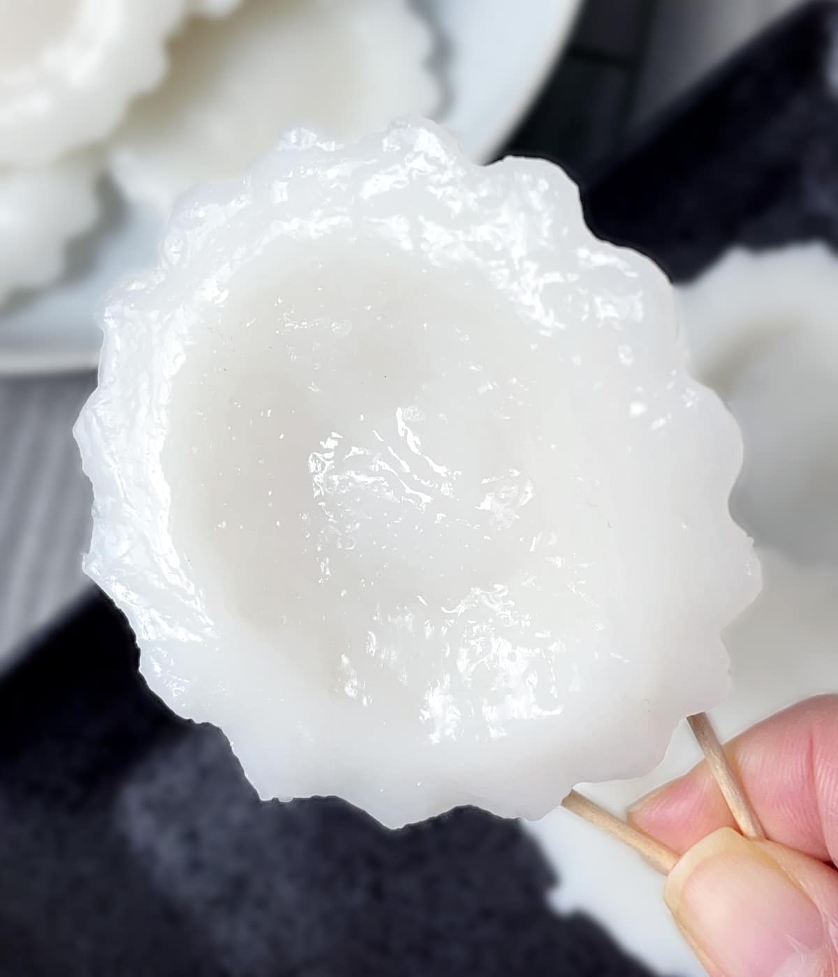 A hand holding toothpicks holding a white round jelly.