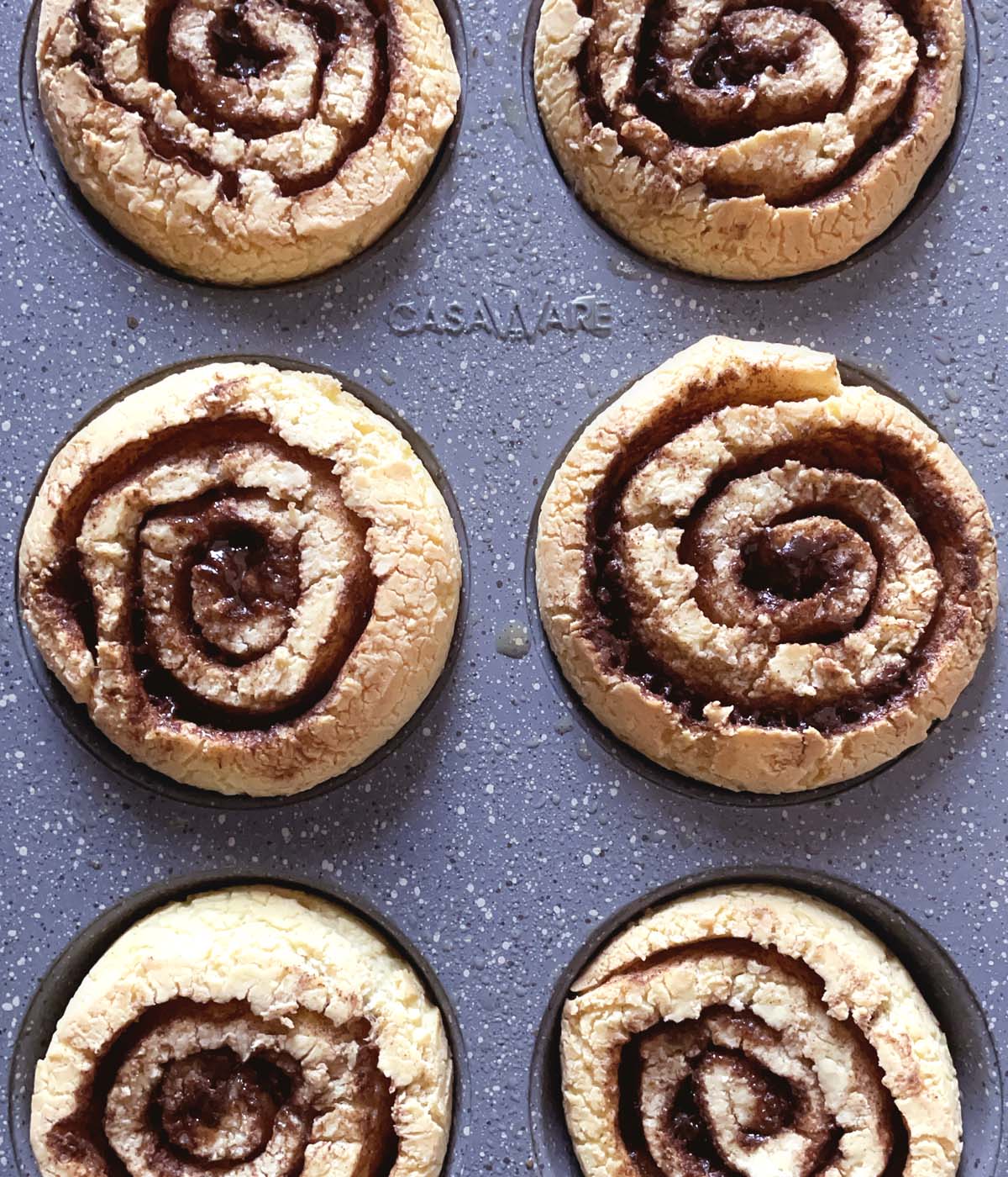 Brown crackled baked cinnamon rolls in a muffin tin.