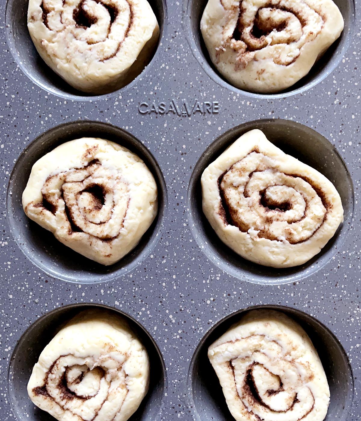 Raw dough cinnamon rolls in a grey muffin tin.