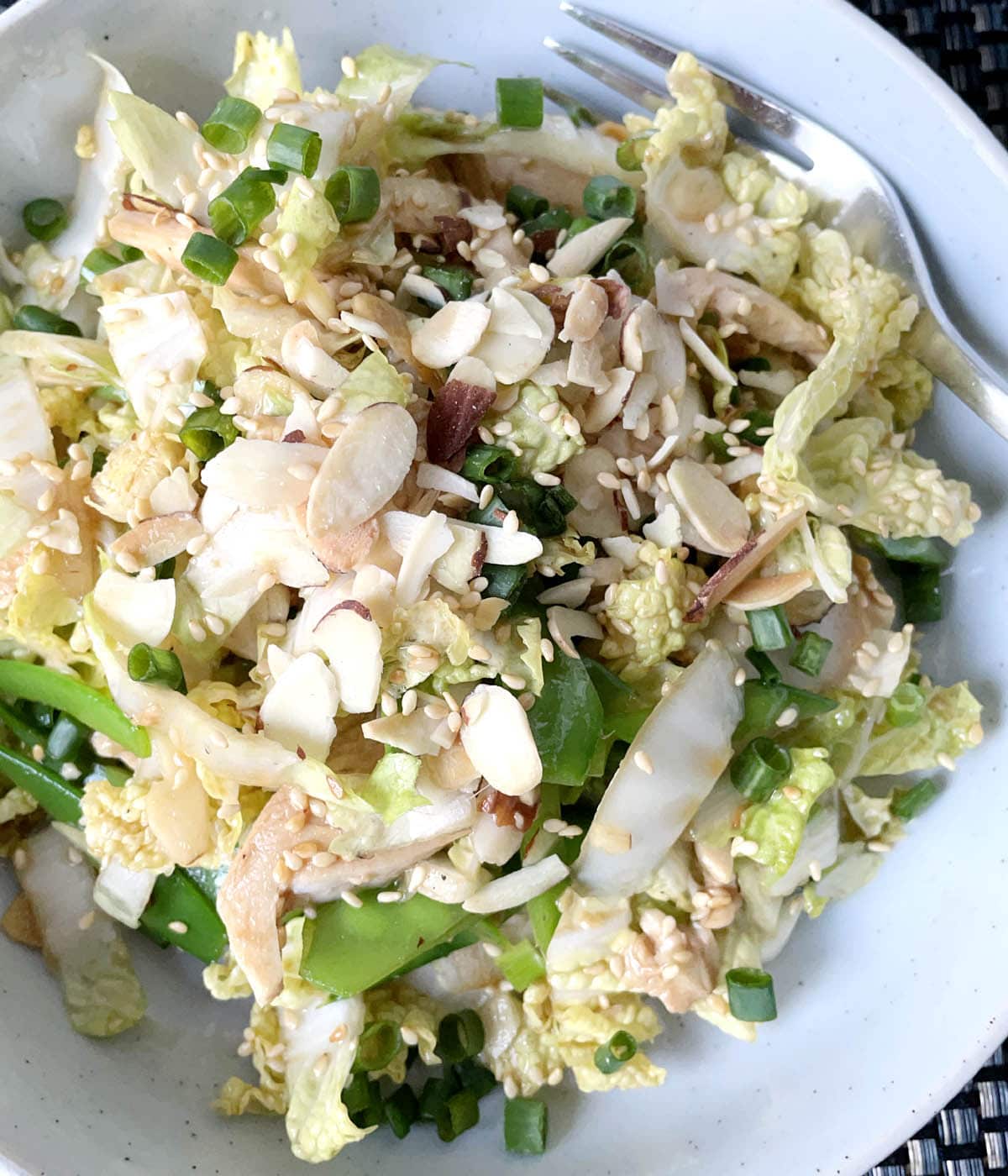 A round white plate containing chicken salad with cabbage and sliced almonds.
