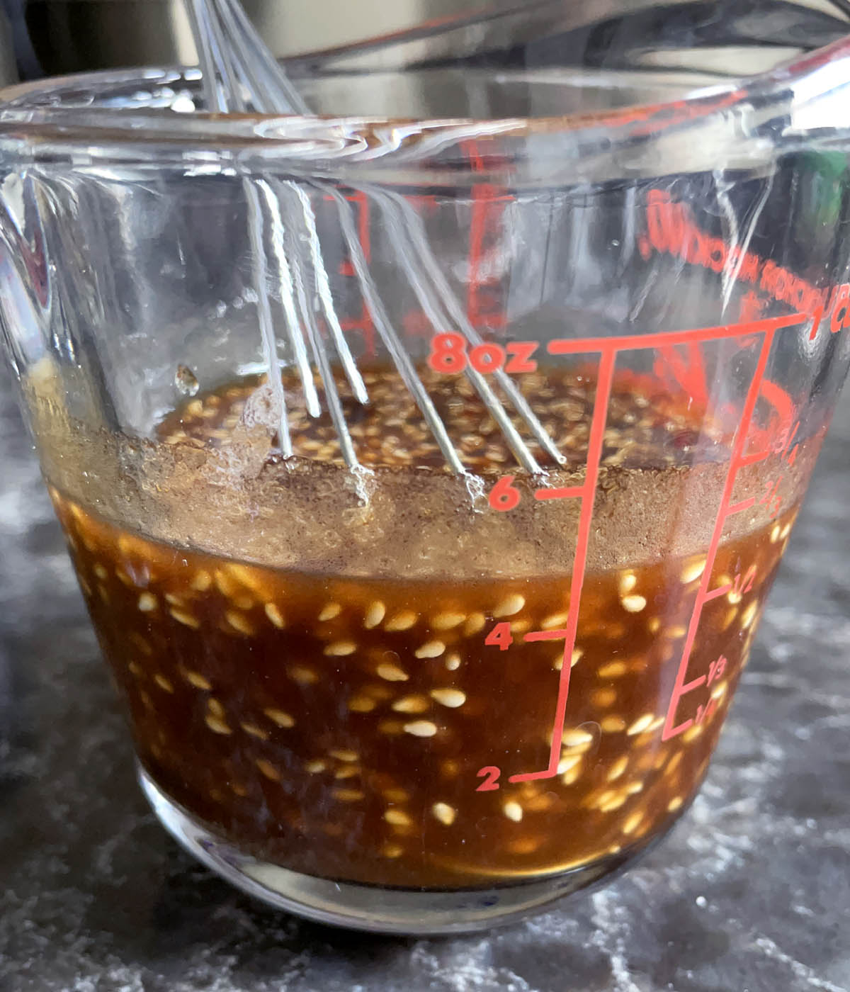 A glass measuring cup containing a thick brown liquid with sesame seeds.