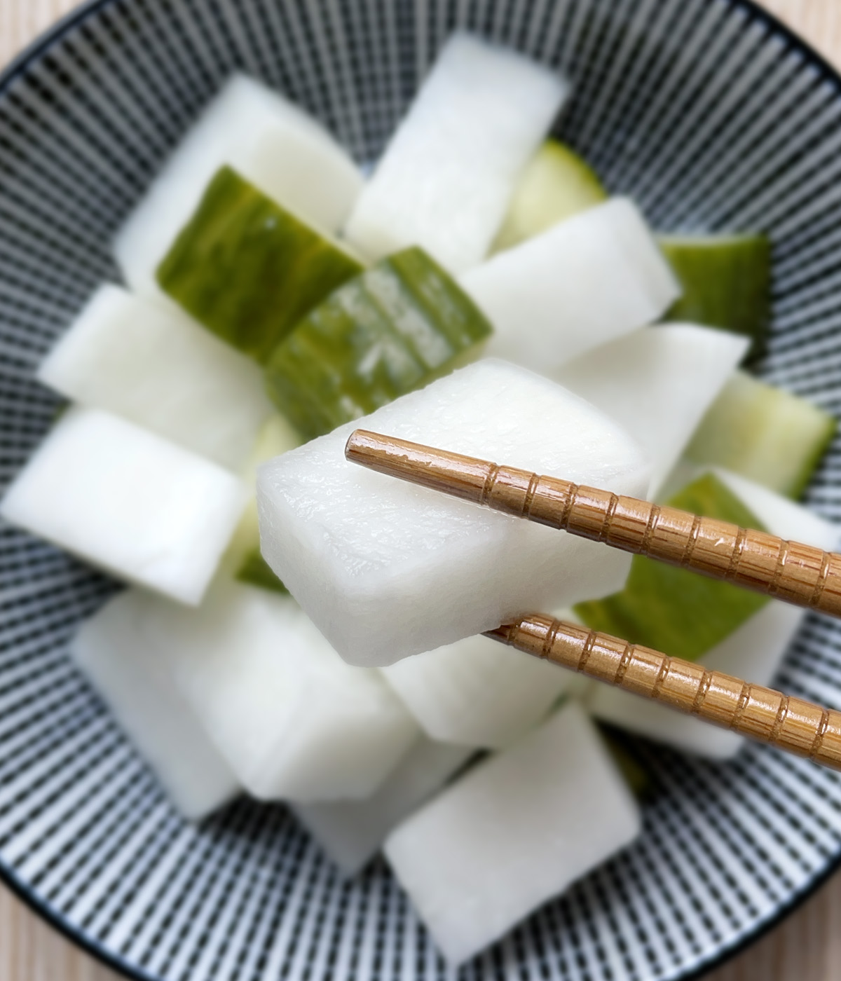 Close-up of a pair of wooden chopsticks holding a chunk of white radish.