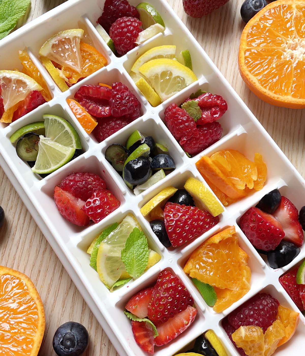 A white ice cube tray filled with various pieces of fresh fruit.