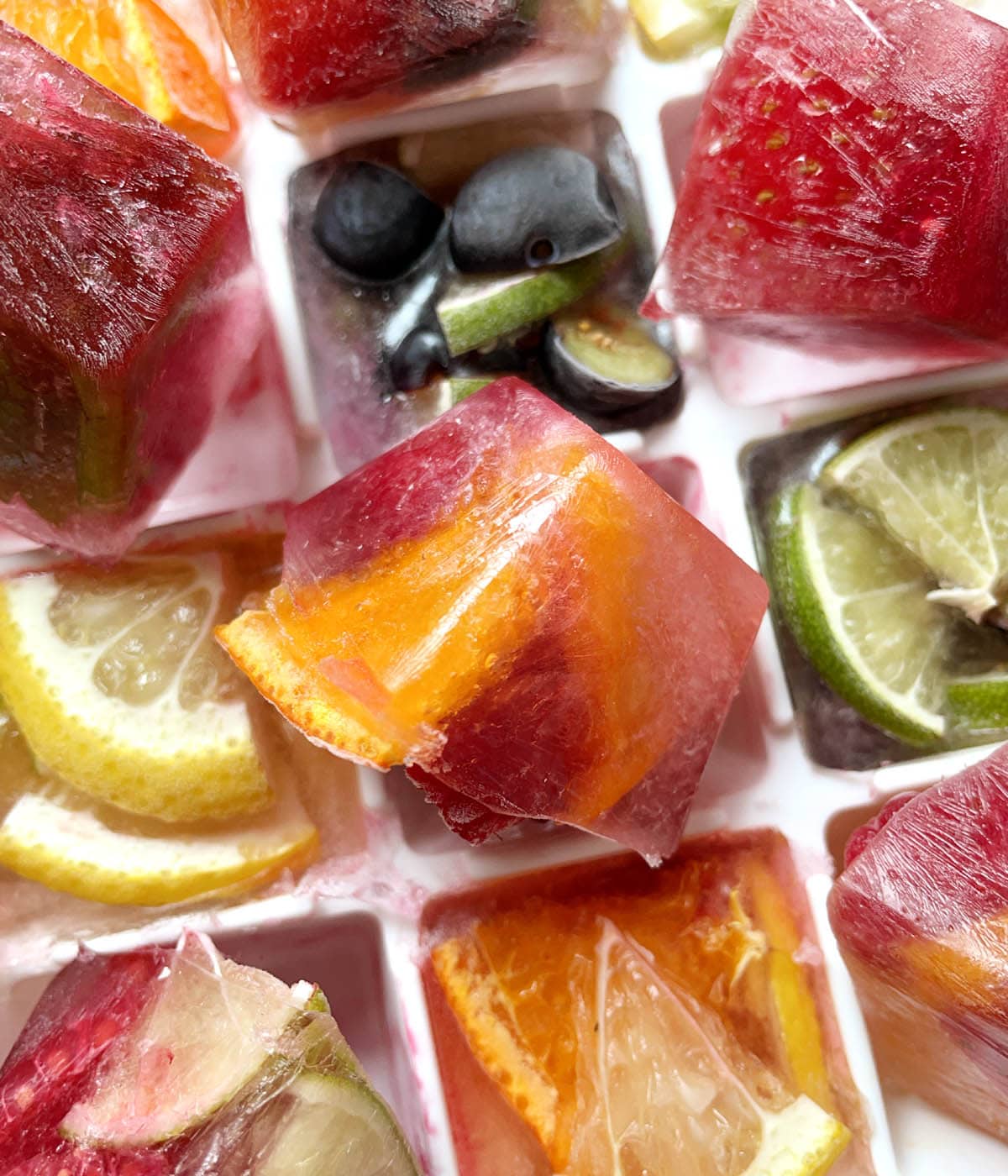 Frozen fruit ice cubes in a white ice cube tray.