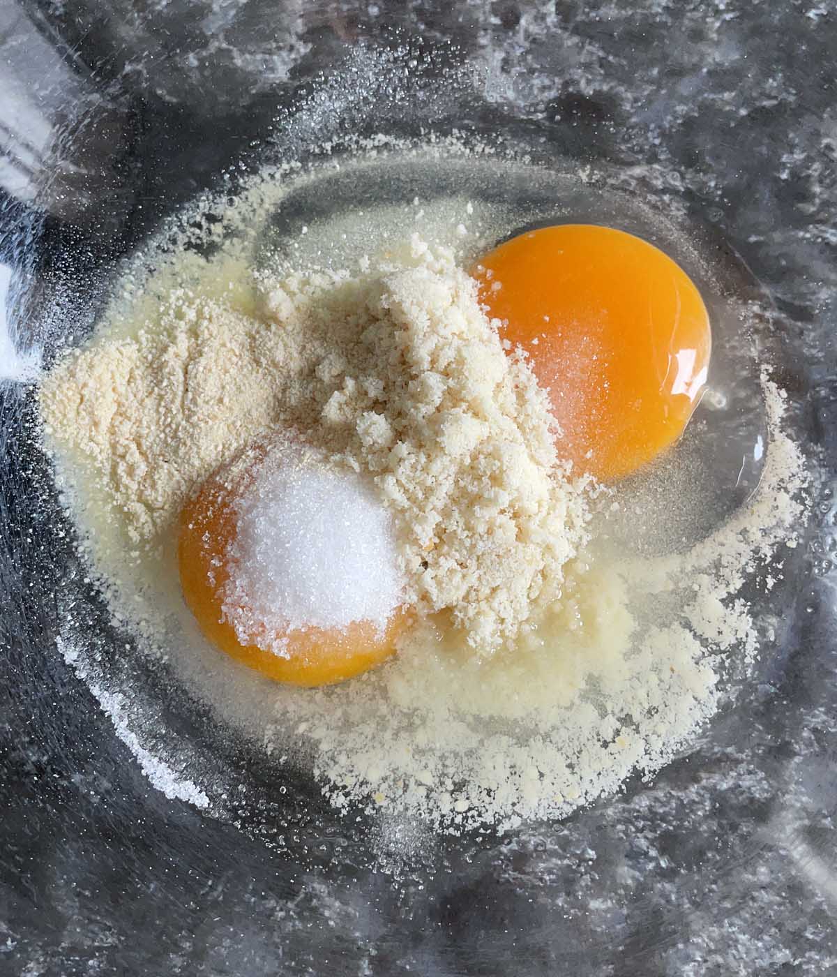 A glass bowl containing two egg yolks and yellow flours.