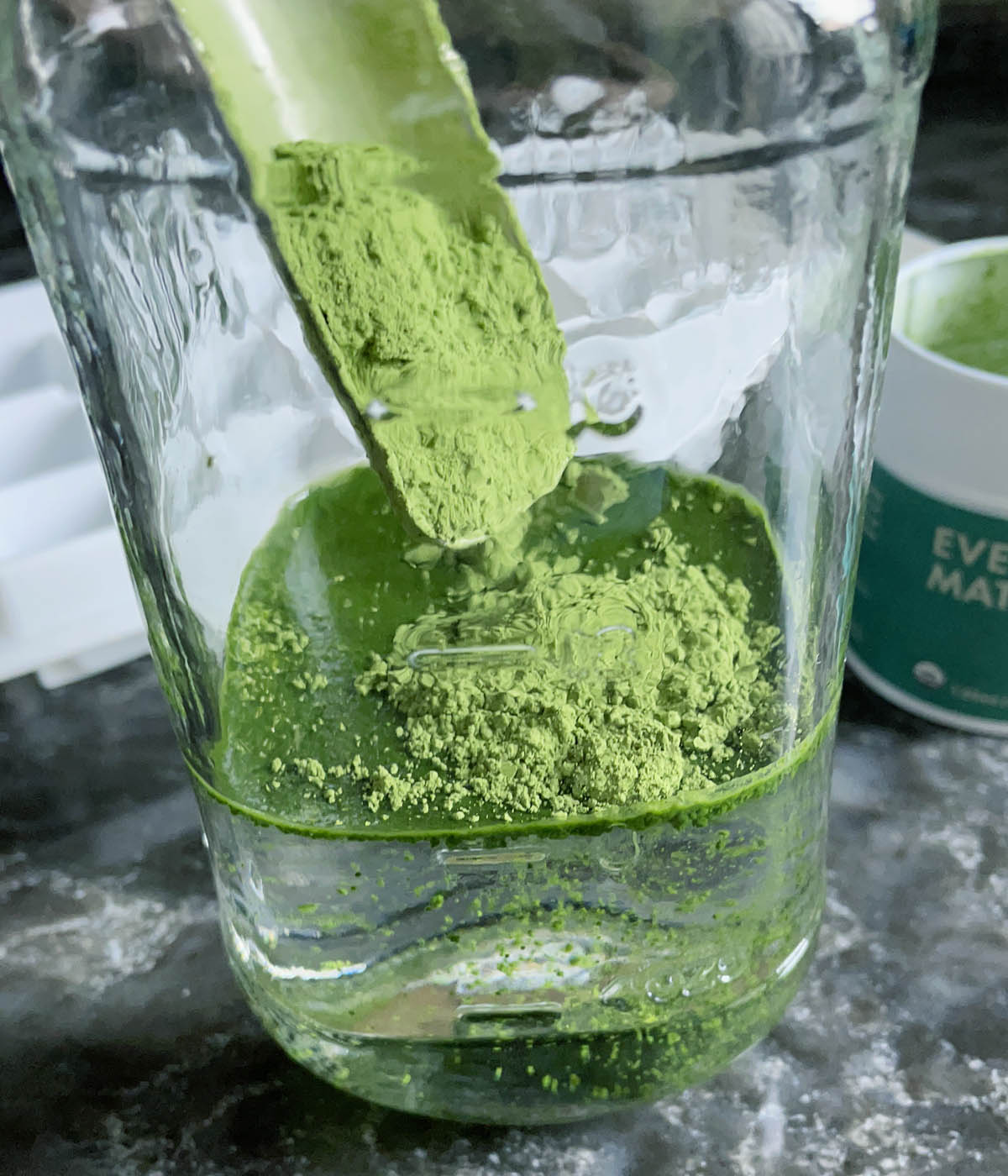 Green powder being added to a glass jar containing water.